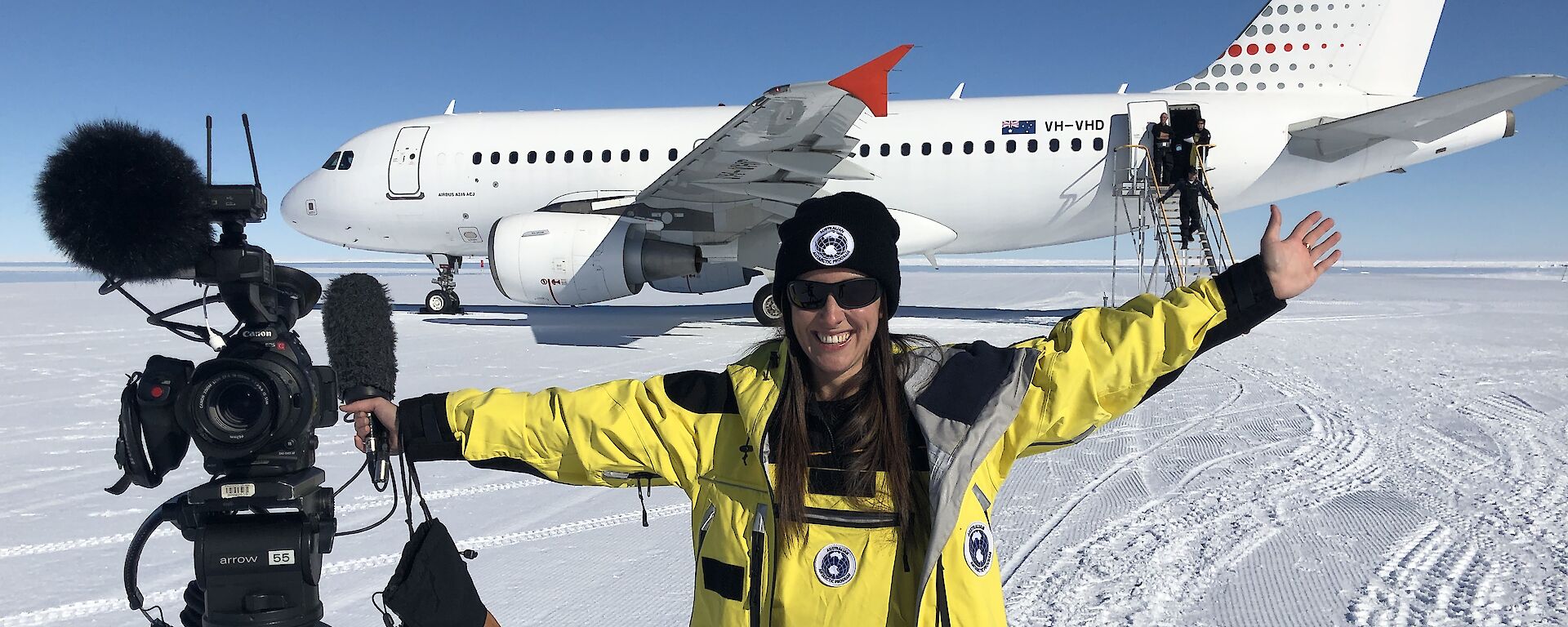 Journalist smiling and posing with camera in front of plane on ice runway,