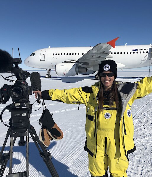 Journalist smiling and posing with camera in front of plane on ice runway,