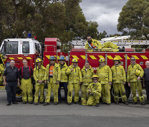 A group of people standing in front of a fire engine wearing yellow protective fireman outfits