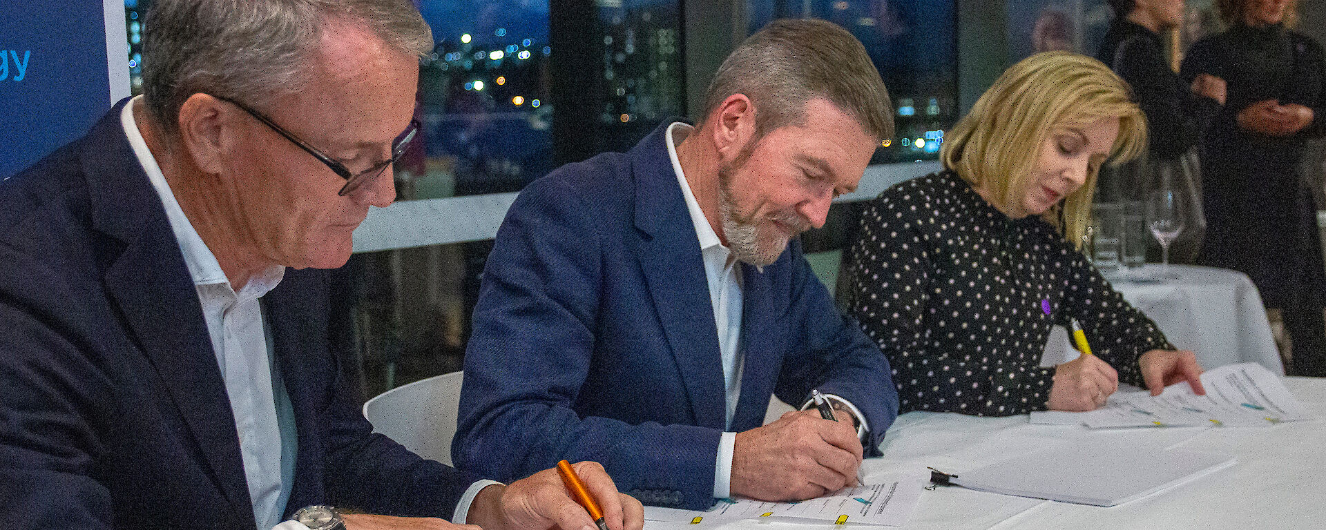 Three people signing paperwork, seated at a table.