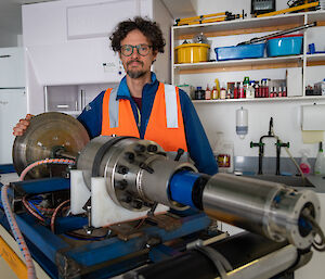 An engineer standing behind a cylindrical stainless steel ice drill component.