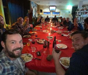 Expeditioners siting around the dinner table decorated with red table cloths and a row of candles up the centre.