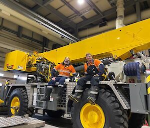 Two expeditioner sitting on the yellow crane with a stuffed toy Border Collie dog in the middle.