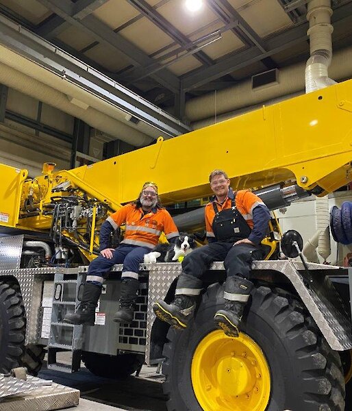 Two expeditioner sitting on the yellow crane with a stuffed toy Border Collie dog in the middle.
