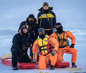 A group photo of five expeditioners resting on the 'rescue alive' platform at the edge of the sea ice.