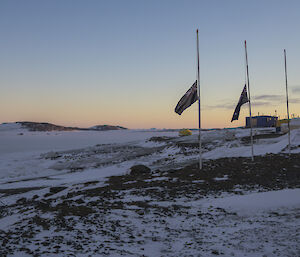 A group of expeditioners gather around the flagpoles at Davis Station for the Anzac Day Dawn Service