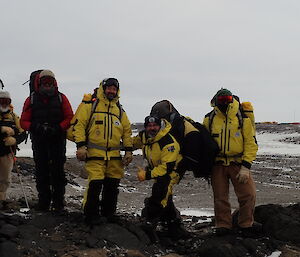 Five people on a hill posing for camera with Davis Station on the horizon in background