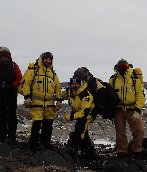 Five people on a hill posing for camera with Davis Station on the horizon in background