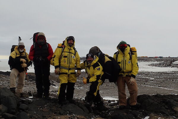 Five people on a hill posing for camera with Davis Station on the horizon in background