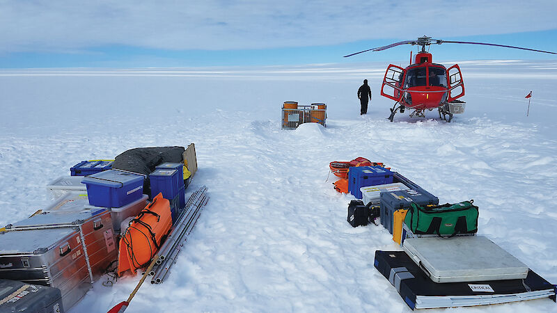 Equipment and a helicopter on a snow-covered glacier in Antarctica.