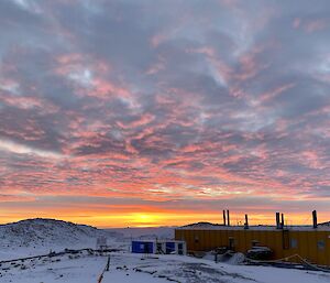 A yellow building in the  snowy foreground with a sunset behind it