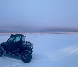 A snow covered panoramic landscape with a quad like vehicle at centre of the shot