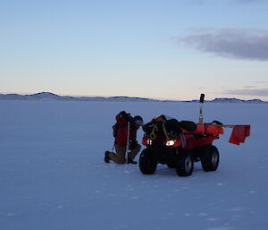 A man kneels on the sea ice drilling to check the depth
