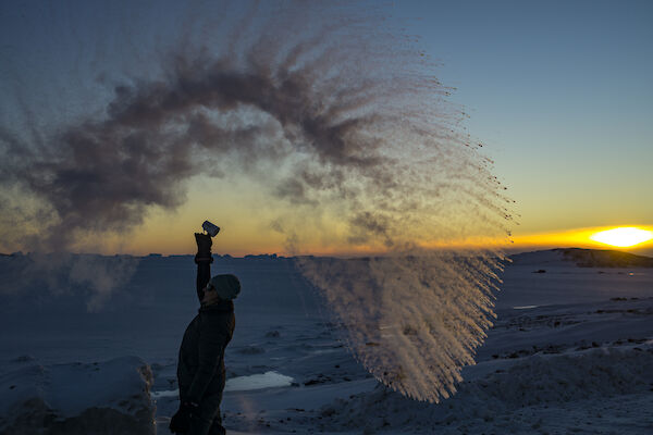 A woman stands in a wave of frozen water against a sunset