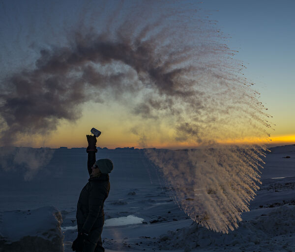 A woman stands in a wave of frozen water against a sunset