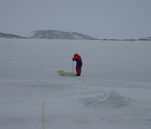 A man out on the sea ice drilling a hole in the ice surface