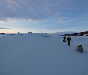 Two expeditioner walking off into the distance, each hauling a sled.