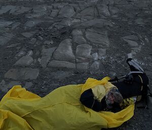 Kate laying in her bright yellow outer bivvy bag on the rocky ground.