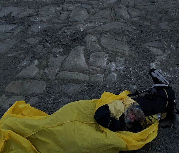 Kate laying in her bright yellow outer bivvy bag on the rocky ground.