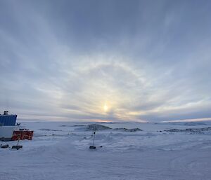 A snowy scene with a cloudy sky in the distance.  A sun halo is peeping through the cloud.