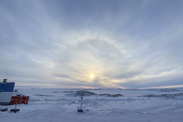 A snowy scene with a cloudy sky in the distance. A sun halo is peeping through the cloud.