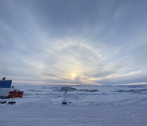 A snowy scene with a cloudy sky in the distance. A sun halo is peeping through the cloud.