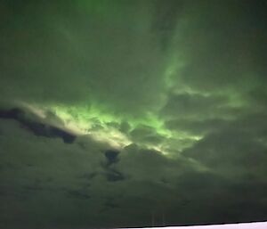 A cloudy night sky coloured green by an aurora australis