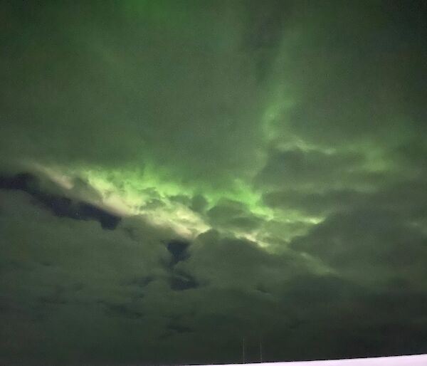 A cloudy night sky coloured green by an aurora australis