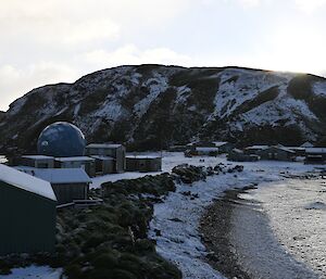 Looking out across some buildings on the shoreline to the snow covered hill behind