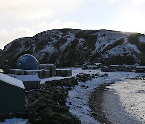 Looking out across some buildings on the shoreline to the snow covered hill behind