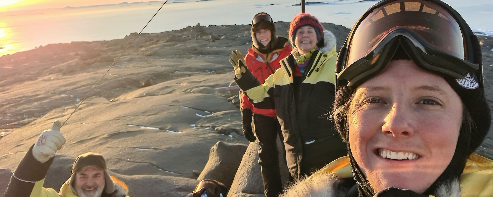 5 Expeditioners on top of the highest point on Beche Island posing for camera with rising sun in the background