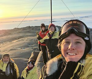 5 Expeditioners on top of the highest point on Beche Island posing for camera with rising sun in the background