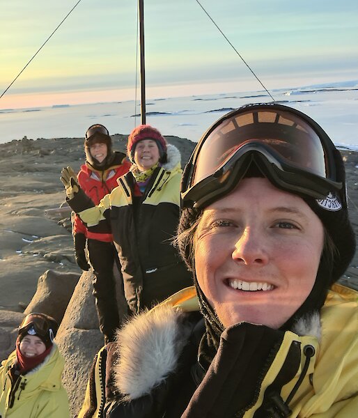 5 Expeditioners on top of the highest point on Beche Island posing for camera with rising sun in the background