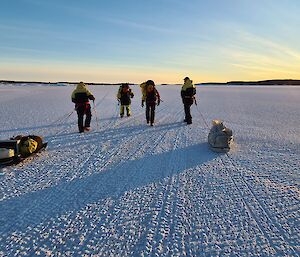 Four expeditioners walking on sea ice towards Beche Island with rising sun in the distance