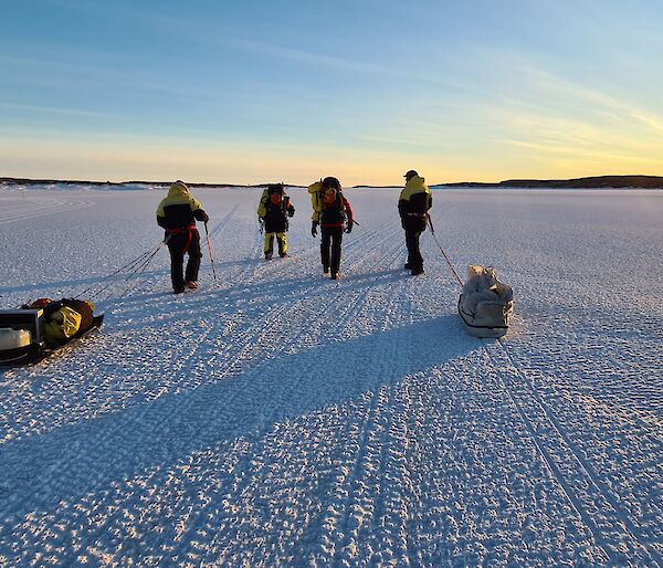Four expeditioners walking on sea ice towards Beche Island with rising sun in the distance