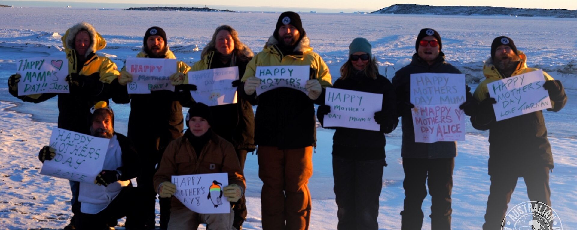 A group of expeditioners standing in the snow holding up Happy Mother's Day signs