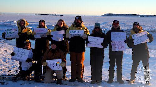 A group of expeditioners standing in the snow holding up Happy Mother's Day signs
