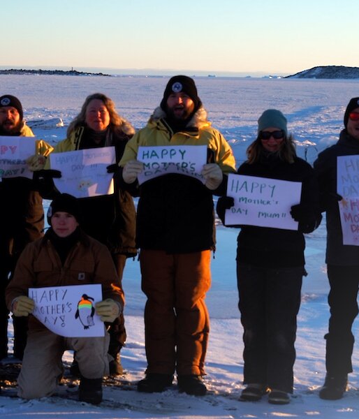 A group of expeditioners standing in the snow holding up Happy Mother's Day signs