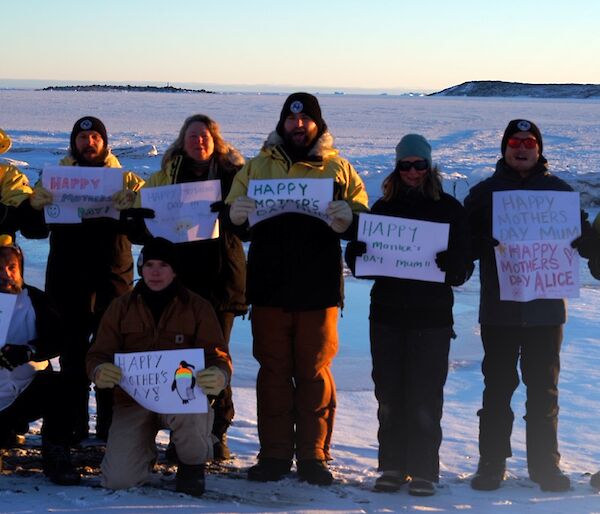 A group of expeditioners standing in the snow holding up Happy Mother's Day signs