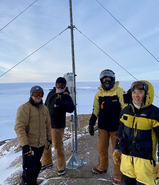 Casey winter expeditioners in a group photo in front an antenna in the snow