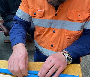 A man is practicing cutting open a tube as a surrogate for a vein