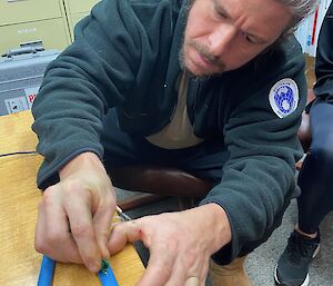 A man is practicing cutting open a tube as a surrogate for a vein