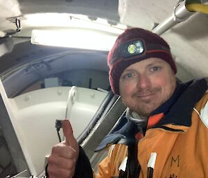 An expeditioner smiles and gives a thumbs up inside the confined space at the top of the wind turbine.