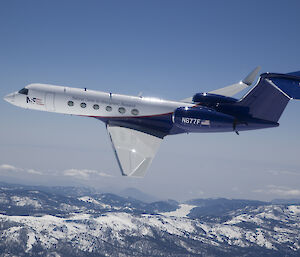 A Gulfstream aircraft over snow capped mountains.