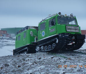 A green Hägglund crests a small hill, pulled by a rope.