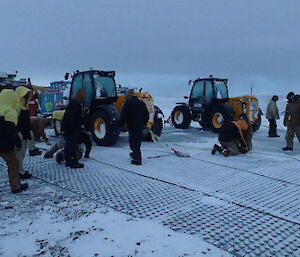 A group of people setting up vehicle winching systems in front on a row of tractors