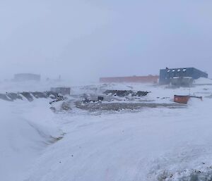 A collection of station buildings with blowing snow all around