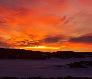 Sun going down in the distance turning the sky and clouds a bright orange and red colour.