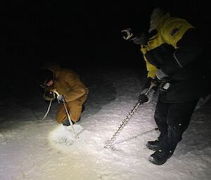2 people working under torchlight to thread a V thread anchor through some ice