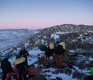 A group of people in hardhats on top of a slope, some attaching ropes to themselves